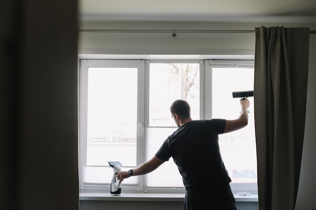 Uomo che lava e pulisce la finestra a casa lavori domestici e pulizie domestiche