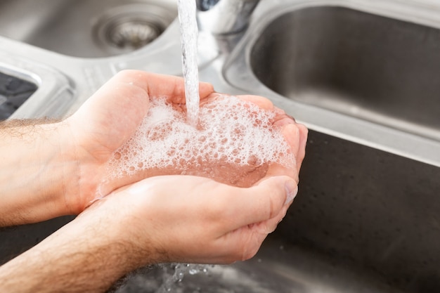 Foto uomo lavarsi le mani con sapone antibatterico e acqua nel lavandino di metallo per la prevenzione del coronavirus. igiene delle mani, assistenza sanitaria, concetto medico. la disinfezione della pelle delle mani protegge da covid 19