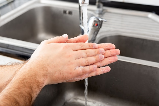 Man washing hands with antibacterial soap and water in metal sink for coronavirus prevention. Hand hygiene.