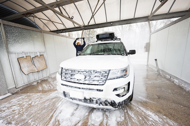 추운 날씨에 셀프 서비스 세차장에서 지붕 선반이 있는 고압수 미국 SUV 자동차를 씻는 남자