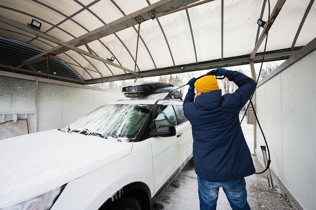 추운 날씨에 셀프 서비스 세차장에서 지붕 선반이 있는 고압수 미국 SUV 자동차를 씻는 남자
