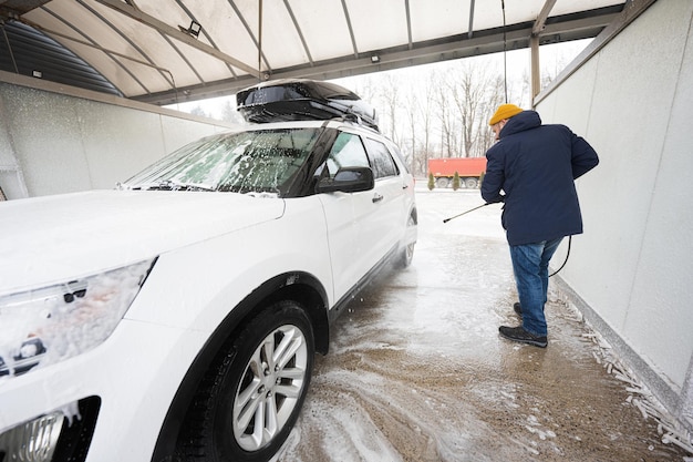 寒い天候下でのセルフサービスウォッシュでルーフラック付きのアメリカのSUV車を高圧水で洗う男