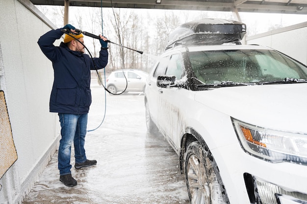 Uomo che lava l'auto suv americana con acqua ad alta pressione con portapacchi al lavaggio self-service a basse temperature