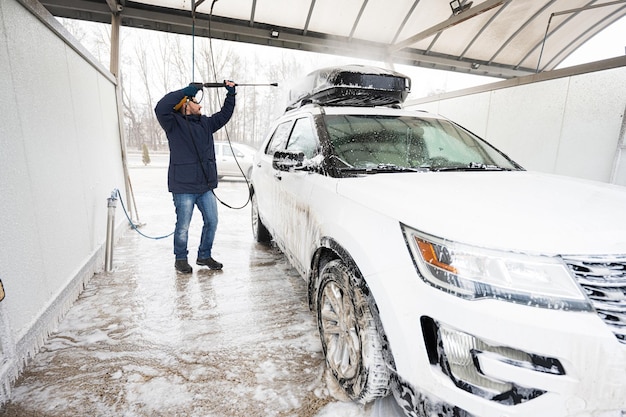 Uomo che lava l'auto suv americana con acqua ad alta pressione con portapacchi al lavaggio self-service a basse temperature