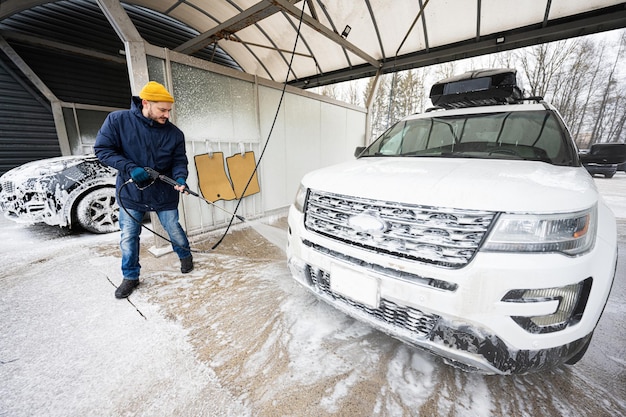 Uomo che lava l'auto suv americana con acqua ad alta pressione con portapacchi al lavaggio self-service a basse temperature