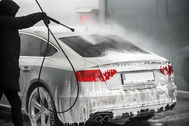 Photo man washing his grey car under high pressure water outdoors. - back view