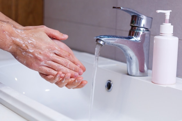 Uomo che si lava le mani in acqua corrente, in un bagno pubblico.
