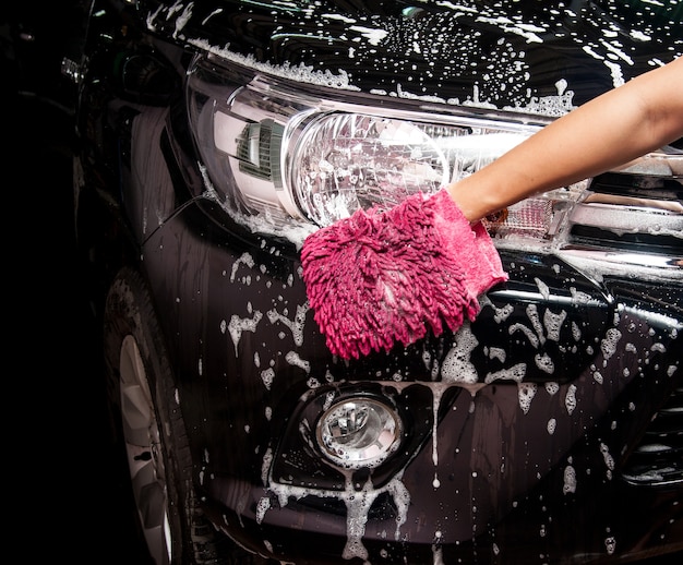 Photo man washing a soapy black car with a cloth