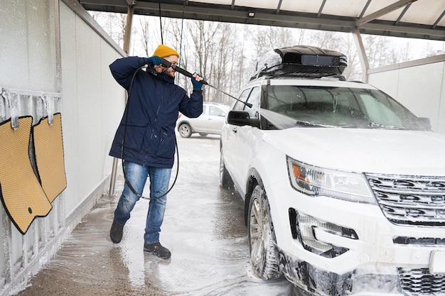 Man wast Amerikaanse SUV-auto met water onder hoge druk met imperiaal bij zelfbediening bij koud weer