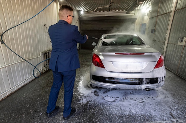 Man wast de auto met hogedrukreiniger Autowasstraat met schuim in autowasstation Een man spuit schuim op de auto met een speciale spray