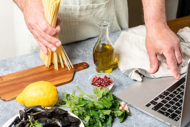 Man watching culinary master class online and learning how to cook spaghetti with seafood mussels