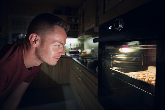 man watching dough in electric oven during baking christmas cookies at home kitchen