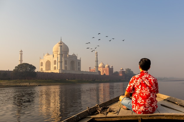 A man watches the sunset over the Taj Mahal from a wooden boat, with a bird soaring overhead.