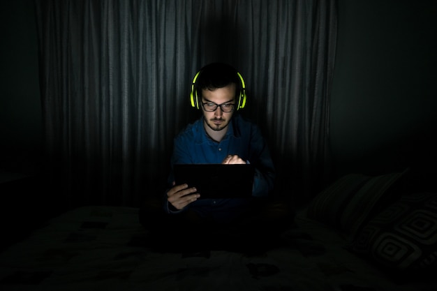 Man watching tv series in a tablet sitting on a bed in the night at home