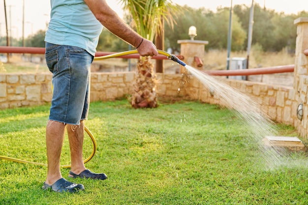 Photo man watering the lawn with a hose in the morning