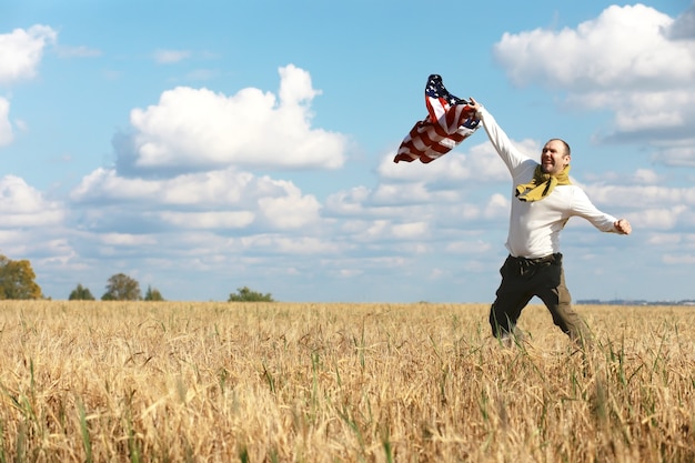牧草地の農地、休日、愛国心、プライド、自由、政党、移民に立っているアメリカの国旗を振る男