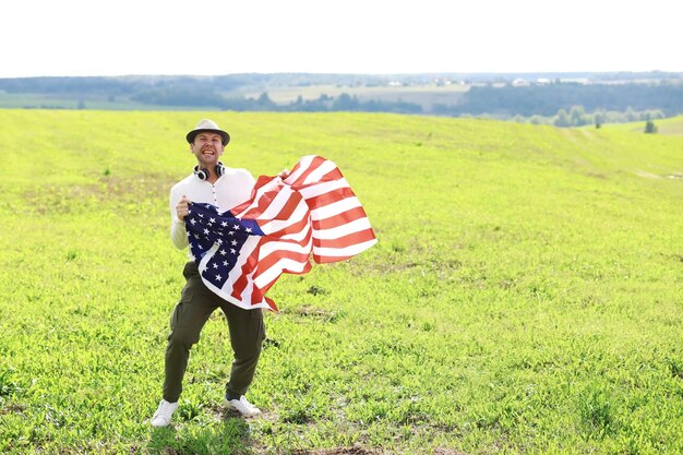 牧草地の農地の休日に立っているアメリカの国旗を振っている男愛国心プライド自由政党移民