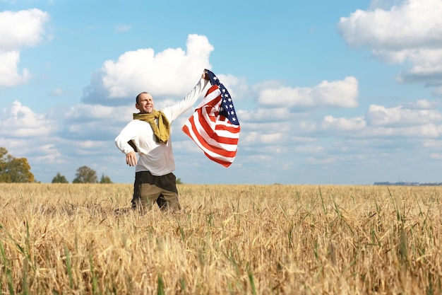 牧草地の農地の休日に立っているアメリカの国旗を振っている男愛国心プライド自由政党移民