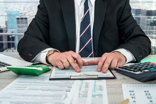 Man wear black suit filling 1040 tax form and using calculator