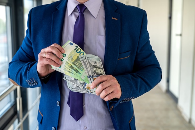 Man wear blue suit holding euro and dollars bills. investment concept