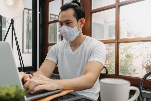 Человек носить маску во время работы со своим ноутбуком в кафе