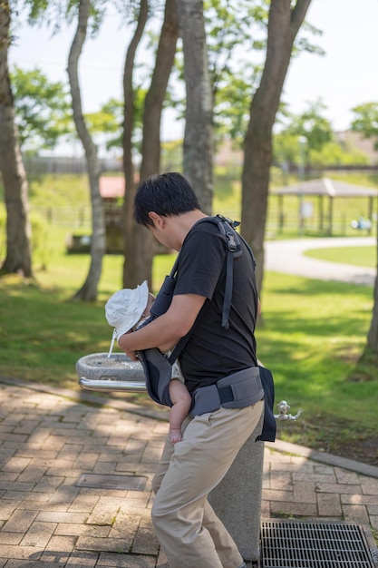 A man wearing a baby carrier is standing in a park.