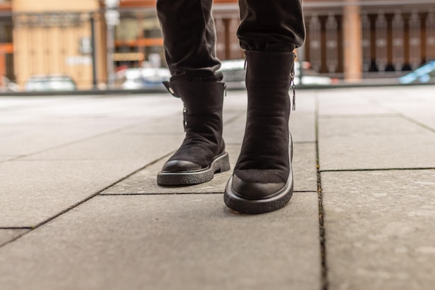 A man wearing black boots stands on a sidewalk.