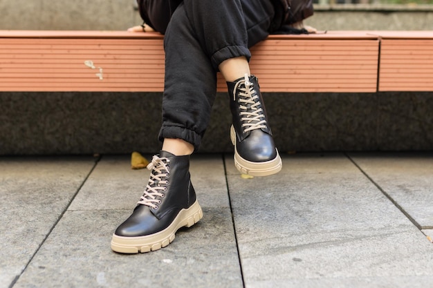 A man wearing black leather shoes sits on a bench.