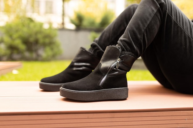 A man wearing a black suede boot sits on a bench in a park.