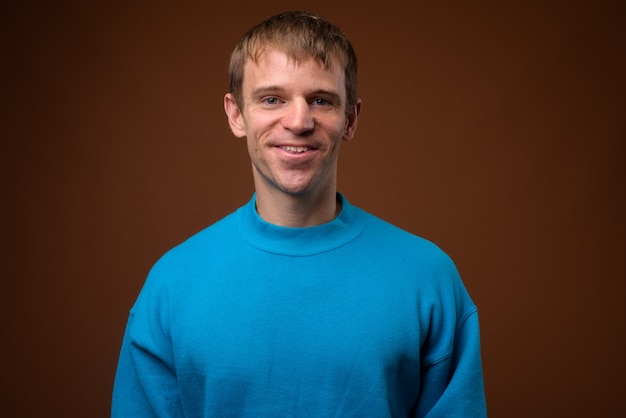 man wearing blue sweater against brown wall