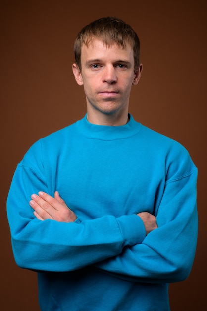 man wearing blue sweater against brown wall