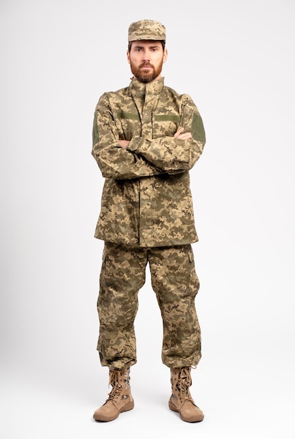 カモフラージュの軍服を着た男ブーツを履き白い背景に孤立した腕を交差させています