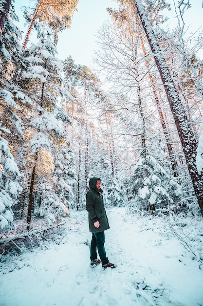 Foto uomo che indossa cappotto e stivali camminando sulla pineta innevata in inverno