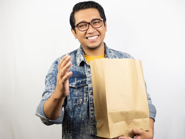 a man wearing glasses and a blue jean jacket holds a paper bag.