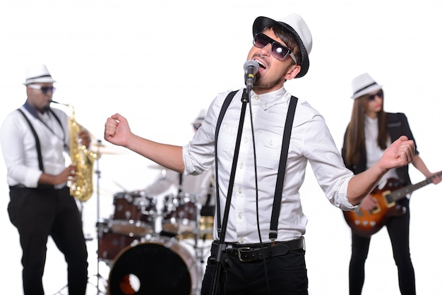 Un uomo con gli occhiali e un cappello canta in un microfono.