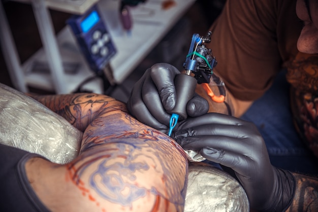 Man wearing gloves showing process of making a tattoo in salon.