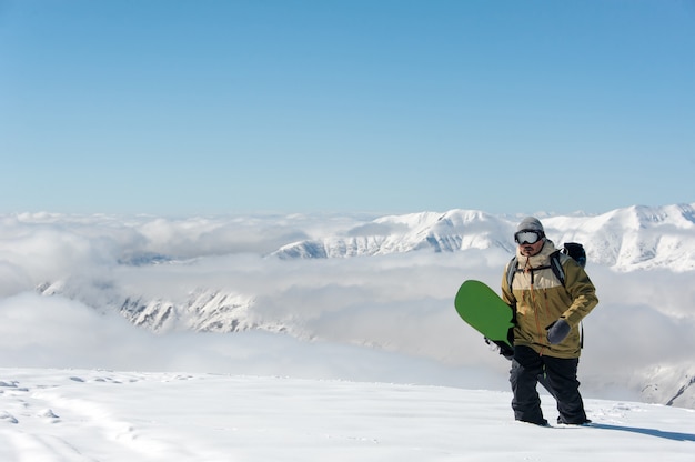 Man wearing goggles and a green snowboard in his hands wanders knee-deep in the snow