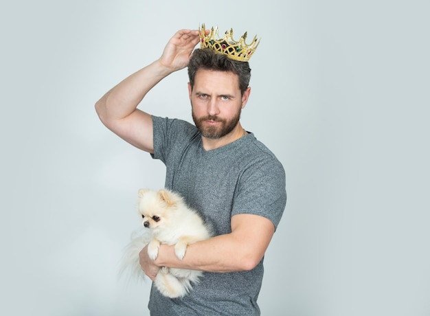 Man wearing golden crown of king hold puppy dog Handsome bearded guy king