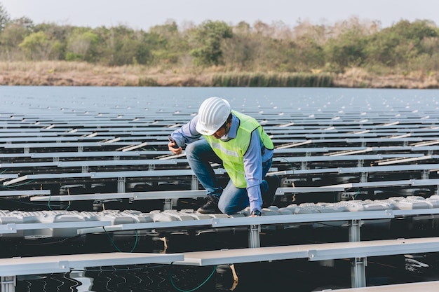 A man wearing a hard hat and a safety vest is kneeling on a floating plant.