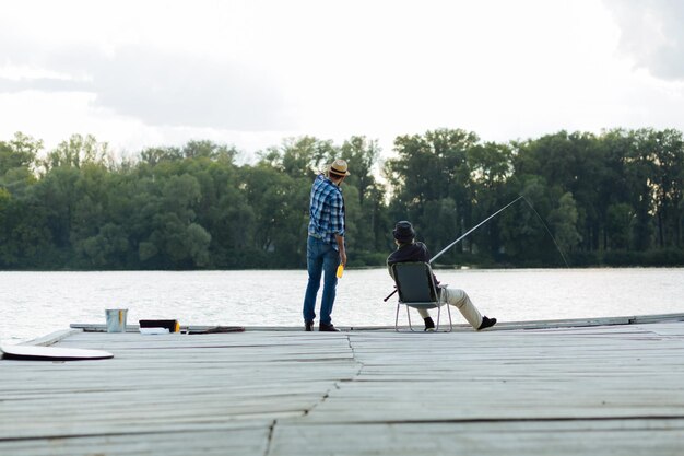 座って魚を捕まえる友人と話している帽子をかぶった男