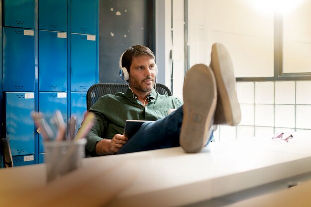 Man wearing headphones working in modern office with feet up on desk