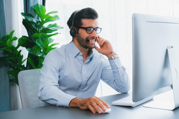 A man wearing a headset sits at a desk with a computer and a monitor that says call center.