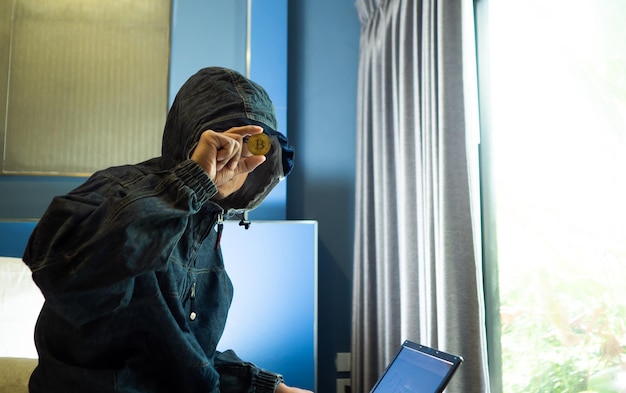 사진 실내에 앉아있는 동안 비트코인을 들고 있는 노트북과 함께 후드 재을 입은 남자