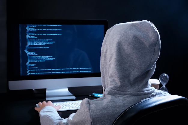 暗い部屋でサーバーをハッキングするパーカーを着た男