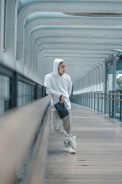 man wearing hoodie posing on pedestrian bridge