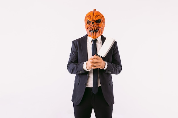 Photo man wearing jacket suit, blue tie and jack-o-lantern pumpkin mask, holding a meat cleaver. halloween and carnival celebration concept.