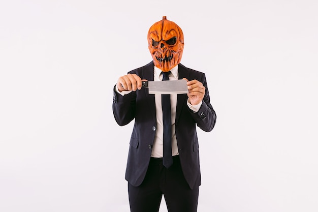Man wearing jacket suit, blue tie and jack-o-lantern pumpkin\
mask, holding a meat cleaver. halloween and carnival celebration\
concept.