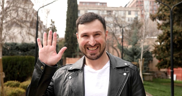 A man wearing a leather jacket waves to the camera.