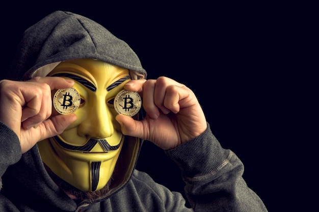 Foto uomo con una maschera che tiene bitcoin su uno sfondo nero