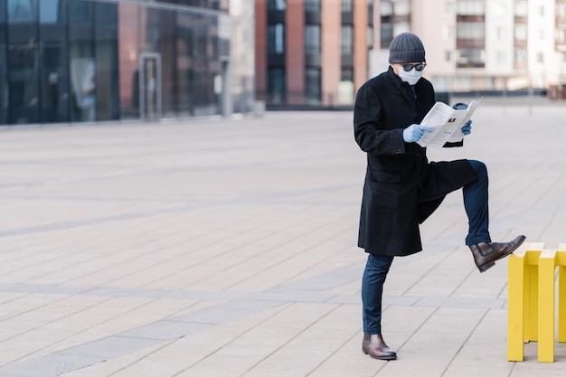 Photo man wearing mask reading newspaper while standing on street